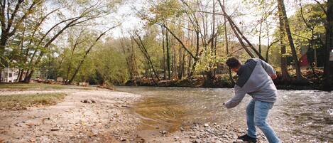 A person standing by a river with trees in the background.