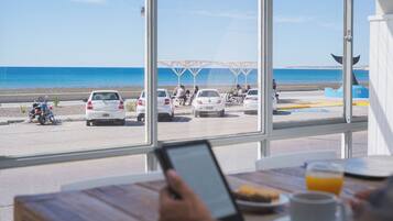 Vista desde una ventana sobre una playa con coches aparcados y gente.