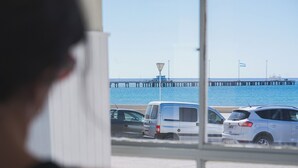 A view through a window of a parking lot with vehicles and a pier extending into the water.