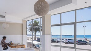 A restaurant with tables and chairs, a view of the beach, and parked cars outside.
