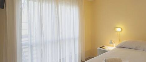 A hotel room with a bed, a nightstand, a lamp, and sheer curtains.
