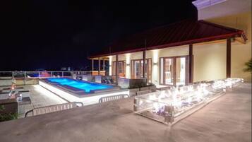 Ein Poolbereich mit Pool, Liegestühlen und einer überdachten Sitzgelegenheit bei Nacht.