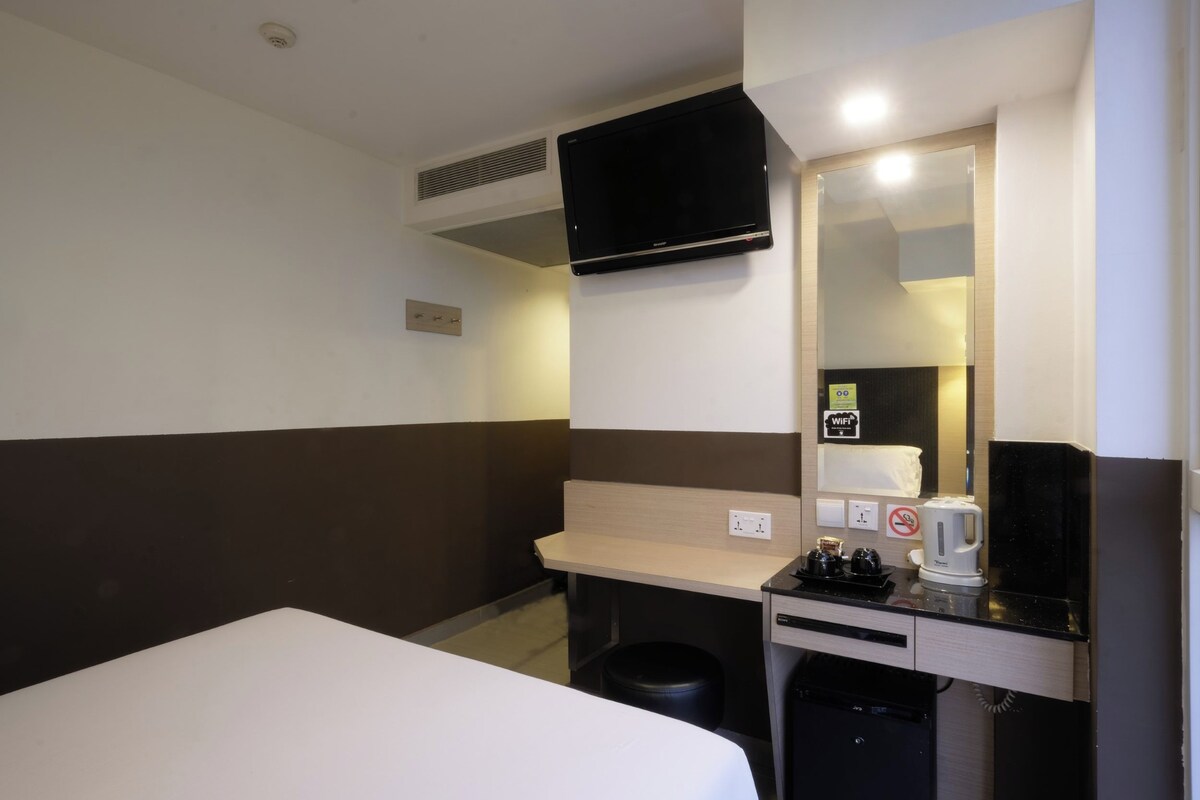 A hotel room with a bed, a desk, a chair, a television mounted on the wall, and a coffee maker.