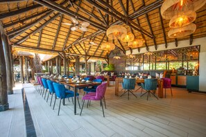 Un restaurante espacioso con techos altos, vigas de madera y sillas coloridas. Las mesas están dispuestas para comer.
