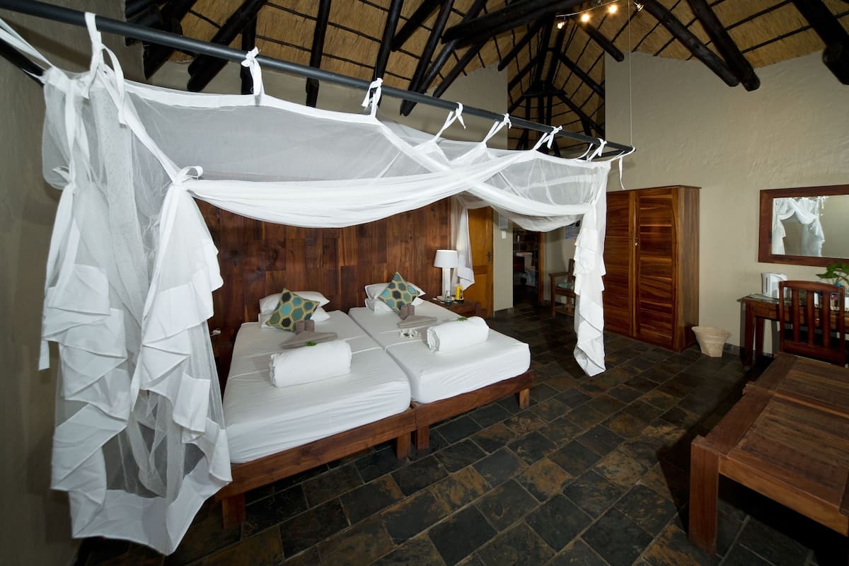 A room with a bed under a canopy, wooden furniture, and a stone floor.