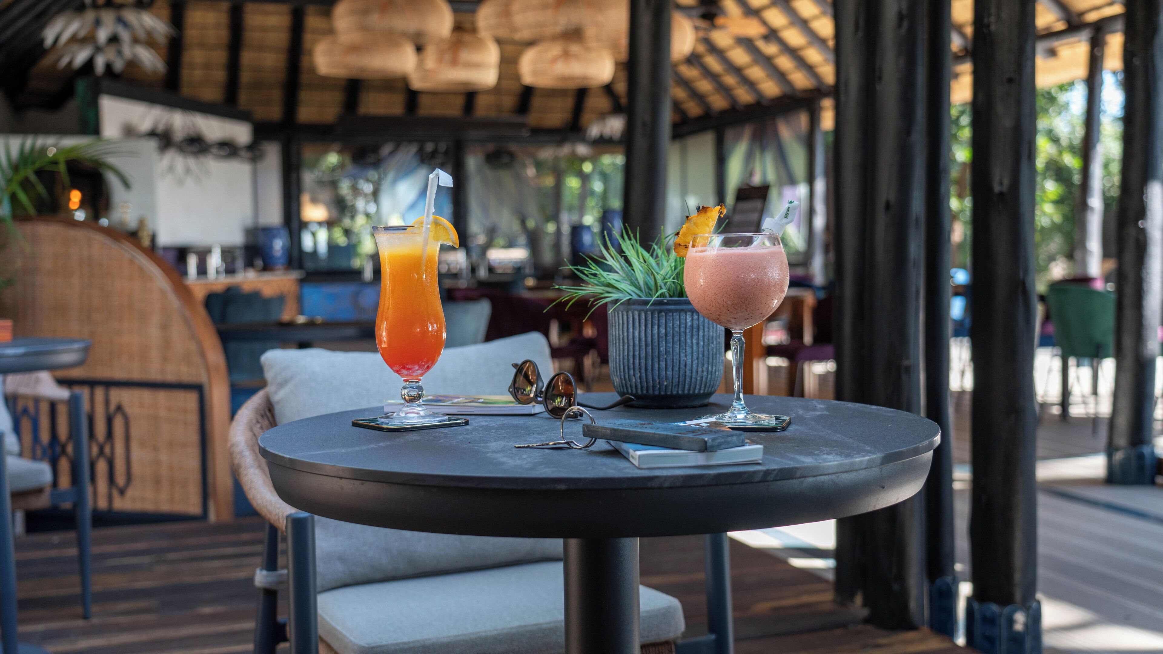A round table with two drinks, a potted plant, and a pair of sunglasses on it.