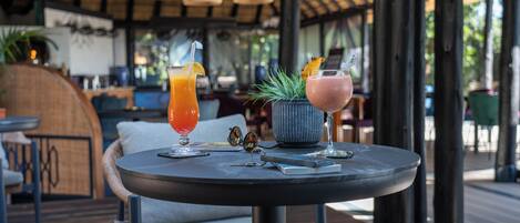 A round table with two drinks, a potted plant, and a pair of sunglasses on it.