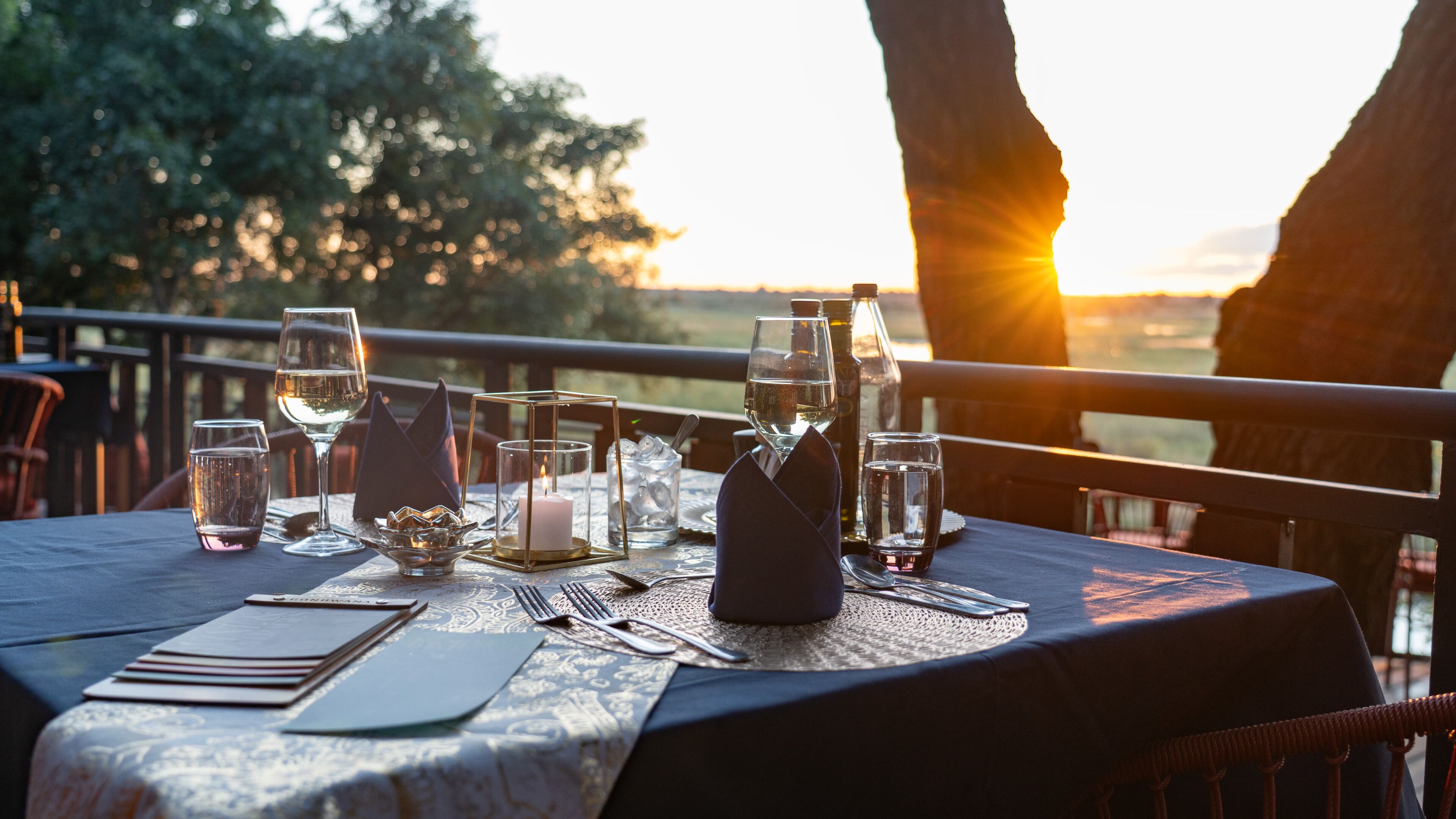 A table set for dining with glasses, a candle, and a bottle, overlooking a scenic view.