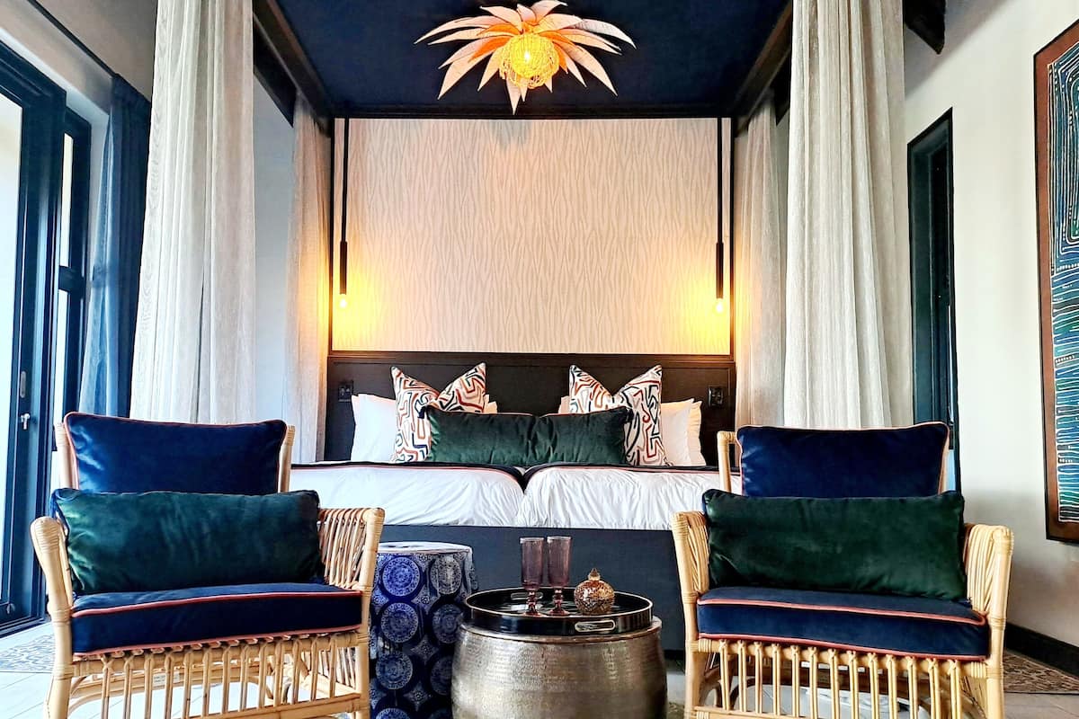A modern bedroom with a large bed, two wicker chairs, a round table, and a decorative ceiling light.