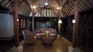 A covered outdoor seating area with wicker furniture, a central round table with a floral arrangement, and a ceiling fan.