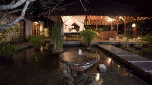 Un jardín tranquilo con un estanque, una zona de estar cubierta y un edificio tradicional con tejado de tejas.