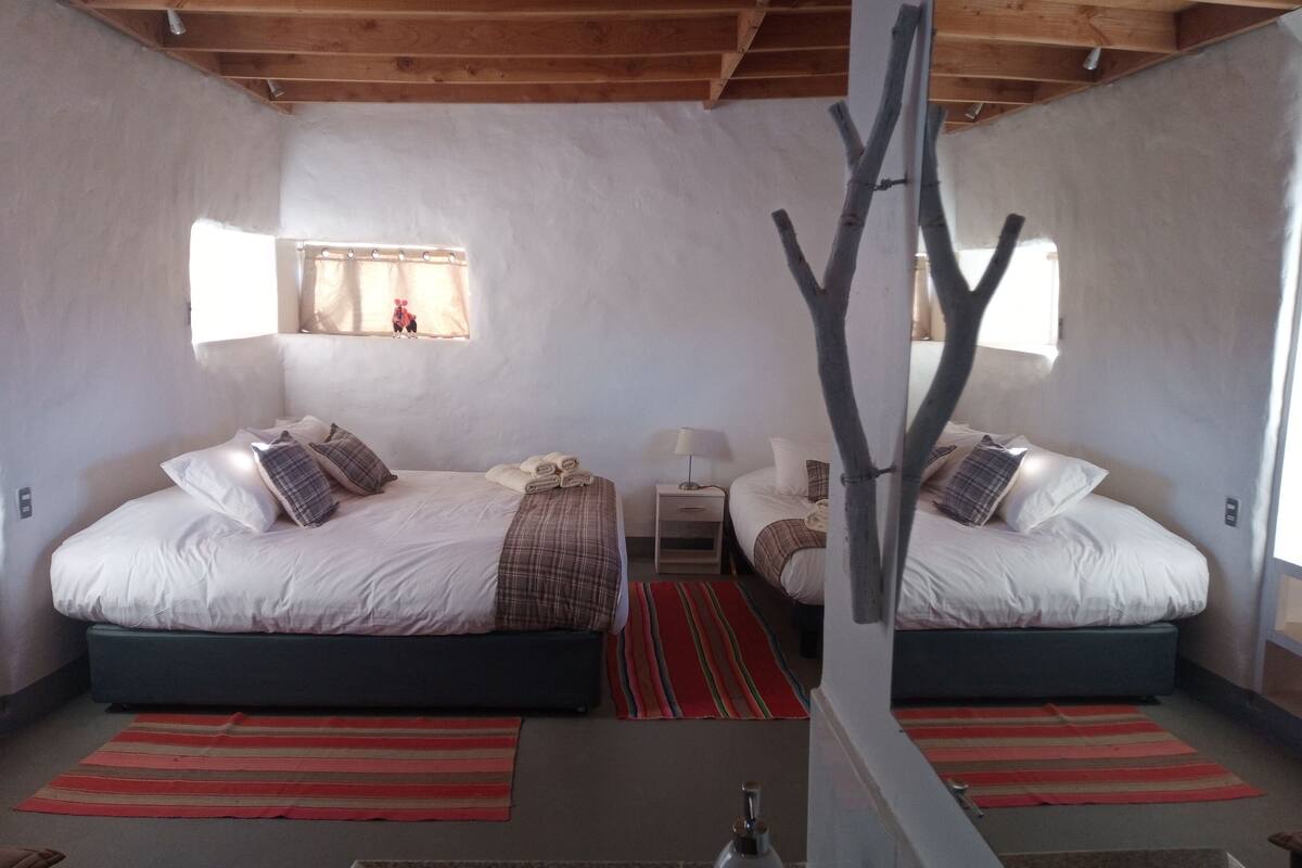 A bedroom with two beds, a window, and a mirror.