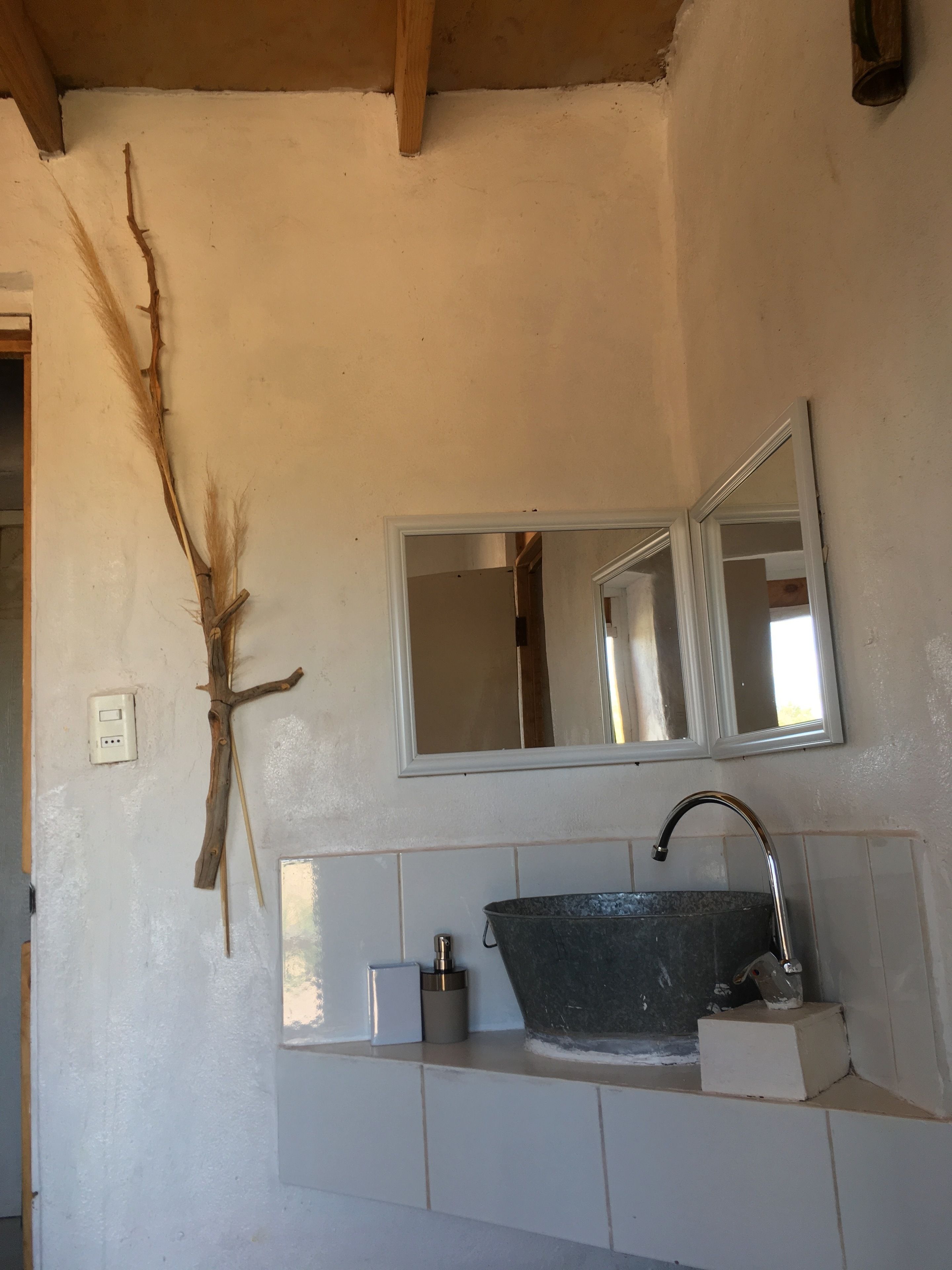 A bathroom with a rustic design, featuring a wooden branch decoration, a large mirror, and a black sink.