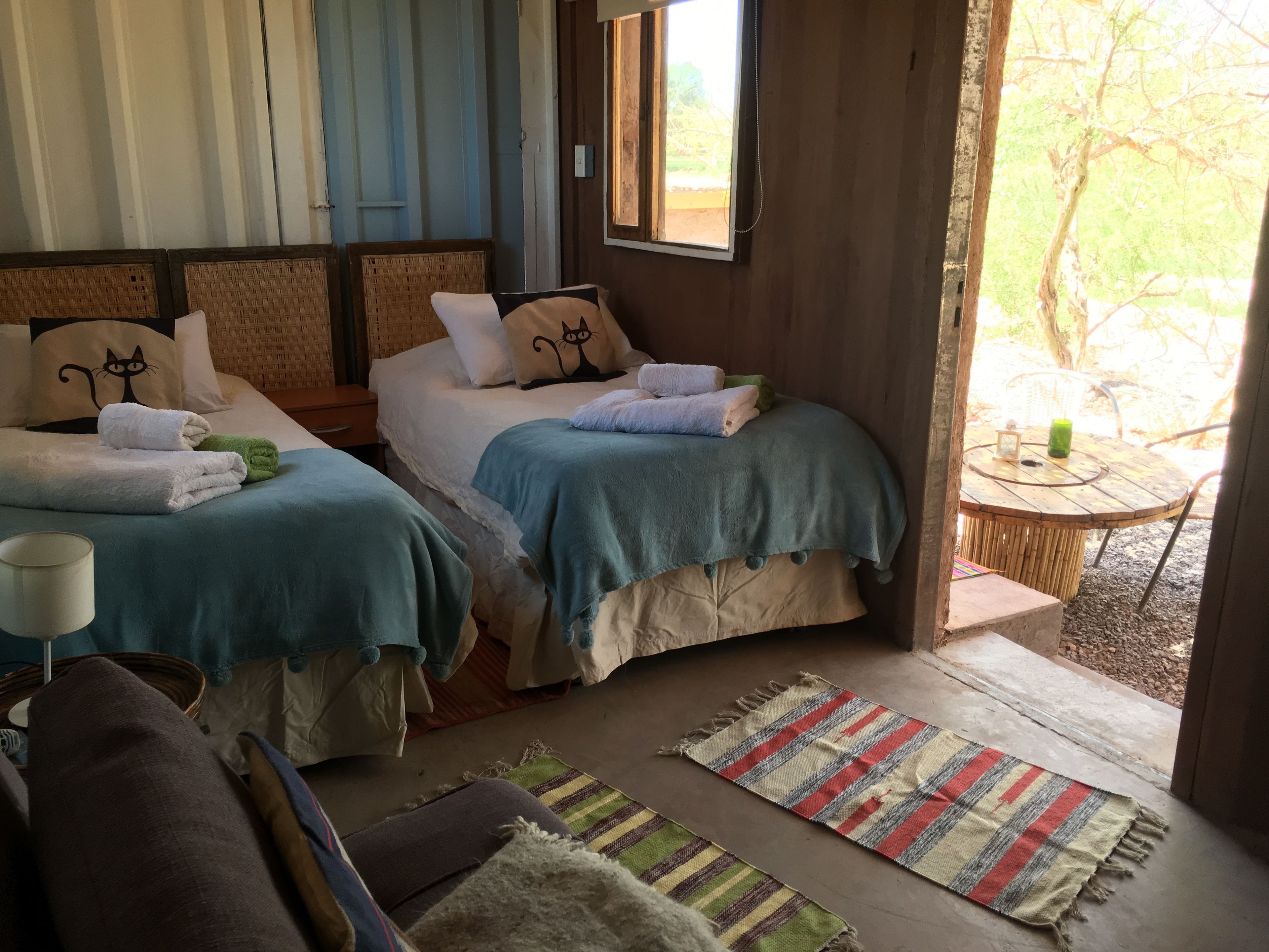 A cozy room with two beds, a small table, and a view of the outdoors.