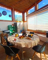 A dining area with a round table, chairs, and a breakfast spread including fruits, juice, and coffee.