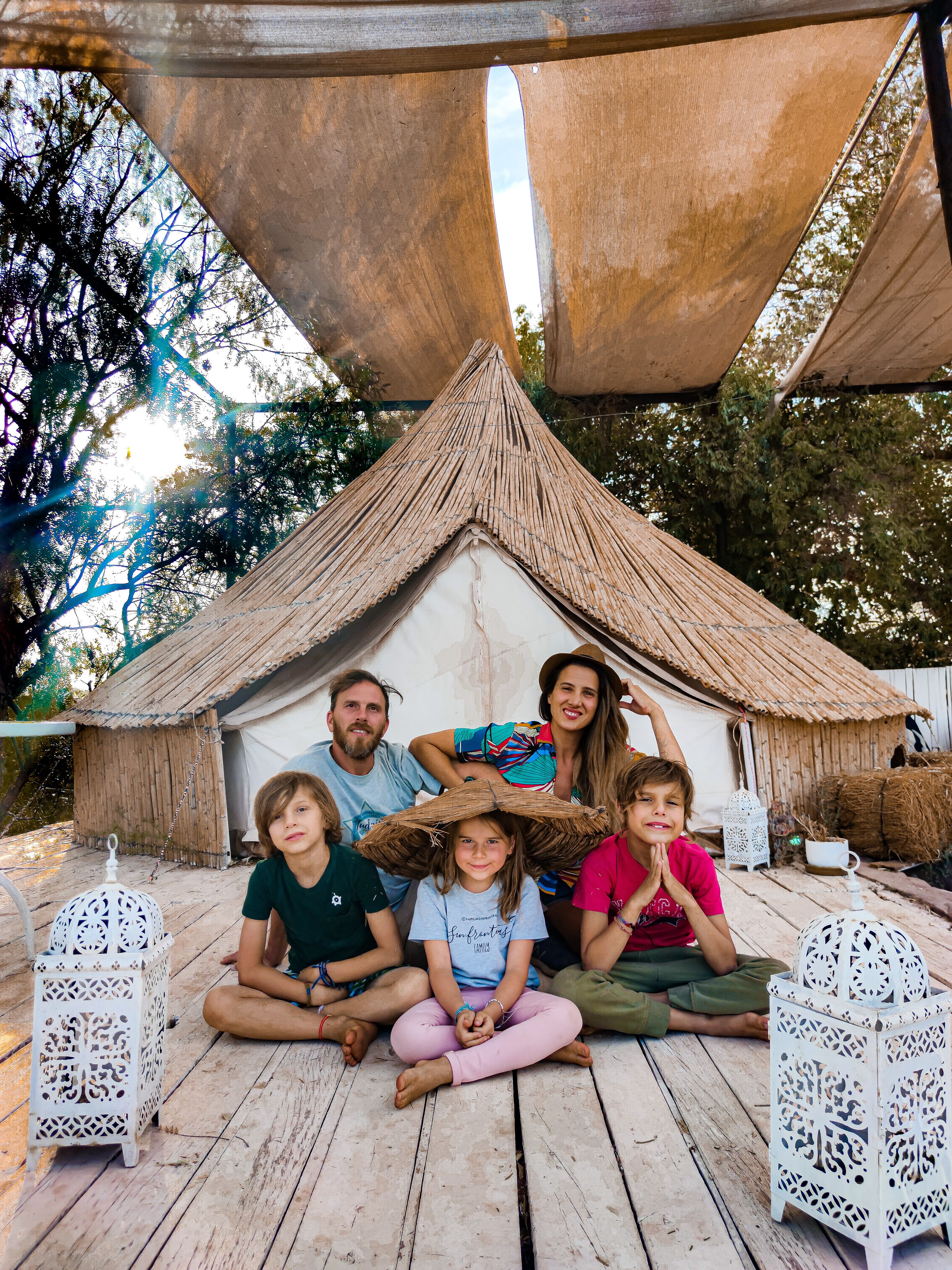 A family sitting under a thatched-roof structure with a wooden deck and white lanterns.