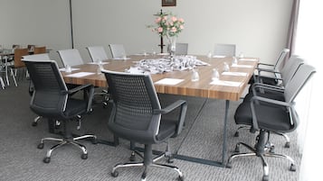 A conference room with a large table, six black office chairs, a vase with pink flowers, and a projector screen.