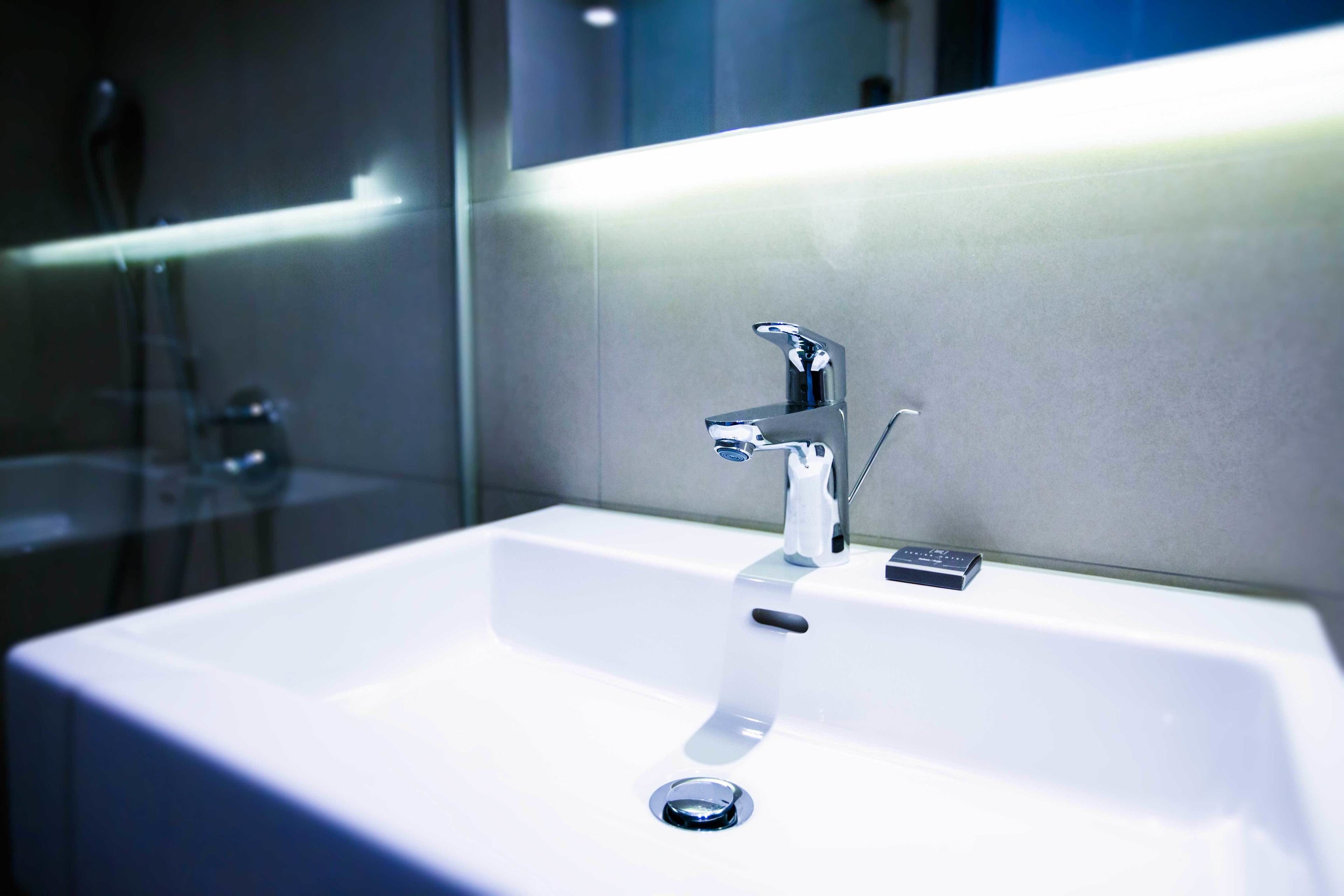 A modern bathroom with a white sink, chrome faucet, and a mirror above it.