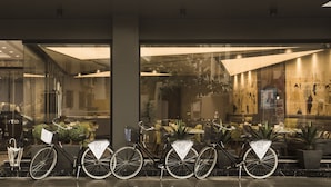A row of bicycles parked outside a building with glass doors, a reception area visible through the doors, and indoor seating with tables and chairs. - Zeniva Hotel (Izmir)