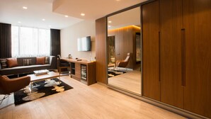 A modern living room with a sofa, coffee table, and a TV. There is a sliding door with a mirror and a wardrobe. - Zeniva Hotel (Izmir)