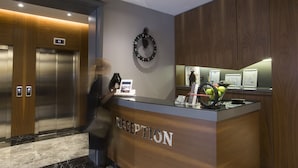 A reception desk with a digital clock, a wall clock, and a fruit bowl. - Zeniva Hotel (Izmir)