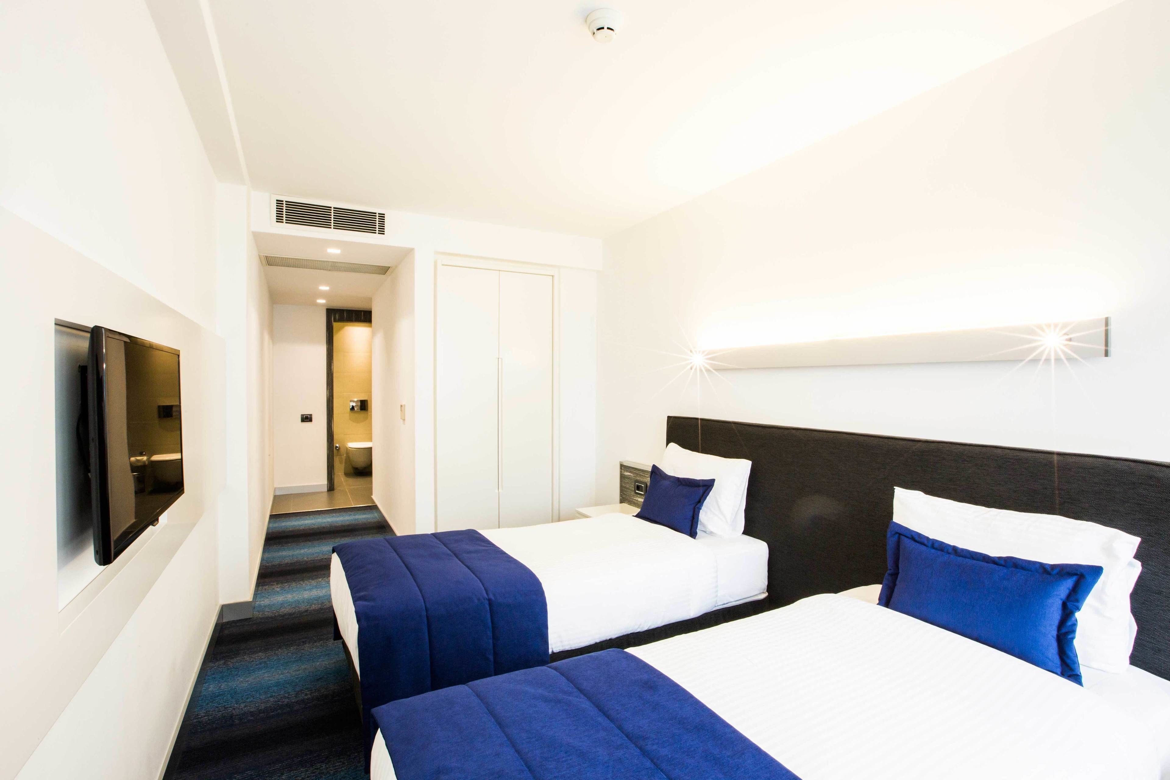 A hotel room with two beds, a TV, and a bathroom visible through an open door.