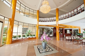 Um hall amplo com arranjo floral central, um lustre imponente e um balcão de recepção.