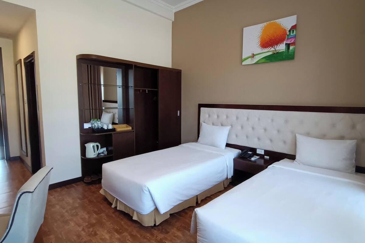 A hotel room with two beds, a wardrobe, a desk, and a painting on the wall.
