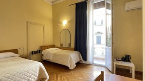 Ein Hotelzimmer mit zwei Betten, Holzboden, einem kleinen Tisch und einem Fenster mit Vorhängen.