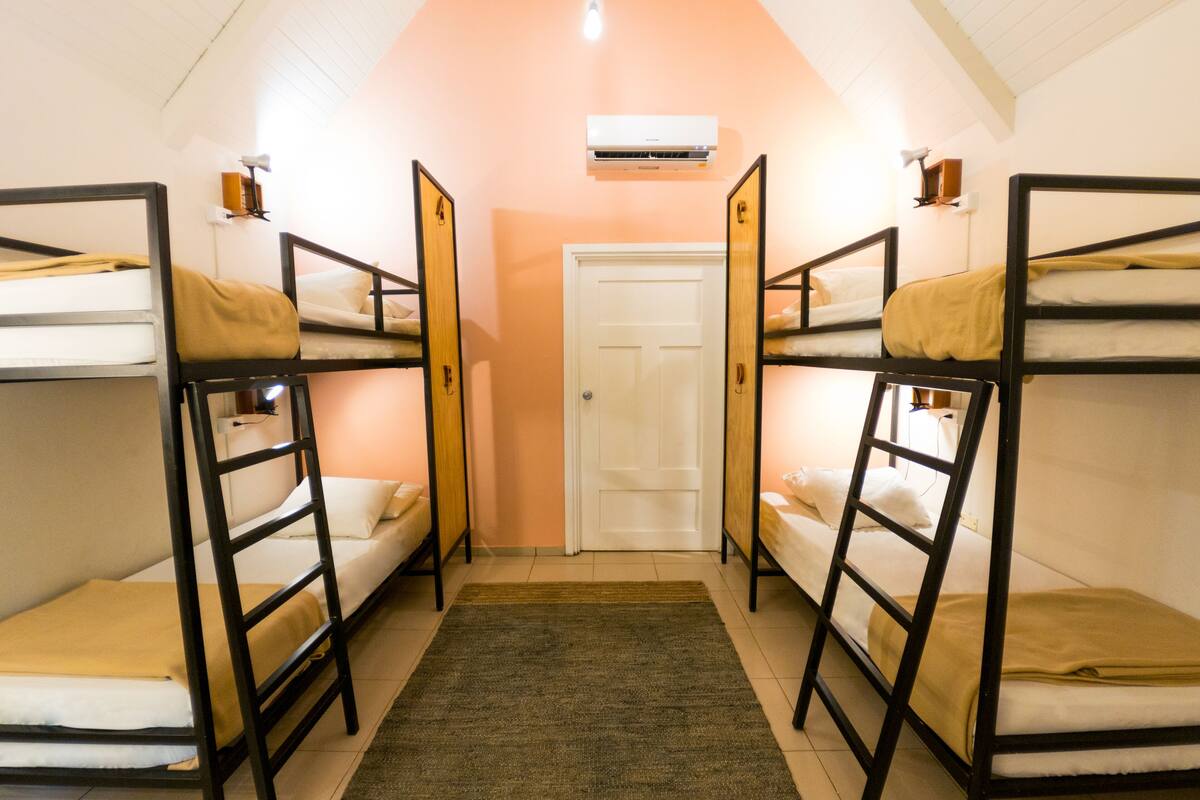 A dormitory room with bunk beds, a door, and an air conditioning unit.