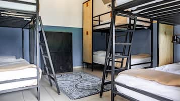 A dormitory room with bunk beds, a wooden ladder, a patterned rug, and a door with a letter 'E' on it.
