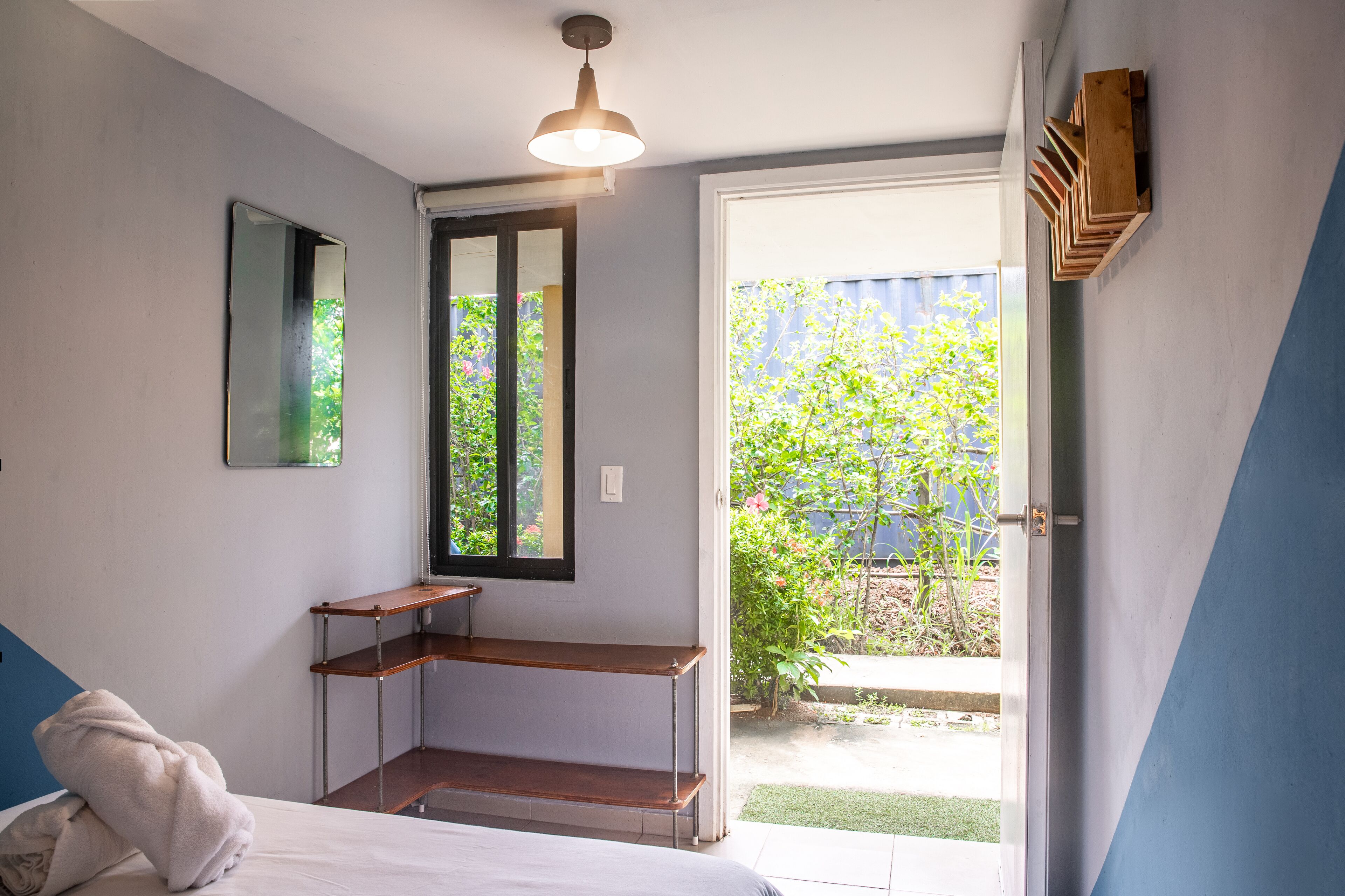 A bedroom with a bed, a bedside table, a mirror, a window, and a door leading to a balcony.