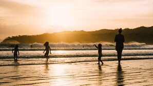A beach scene with people walking along the shore during sunset.