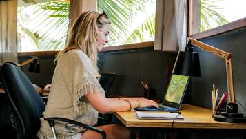Une personne est assise à une table en bois, devant un ordinateur portable, un carnet et une lampe.