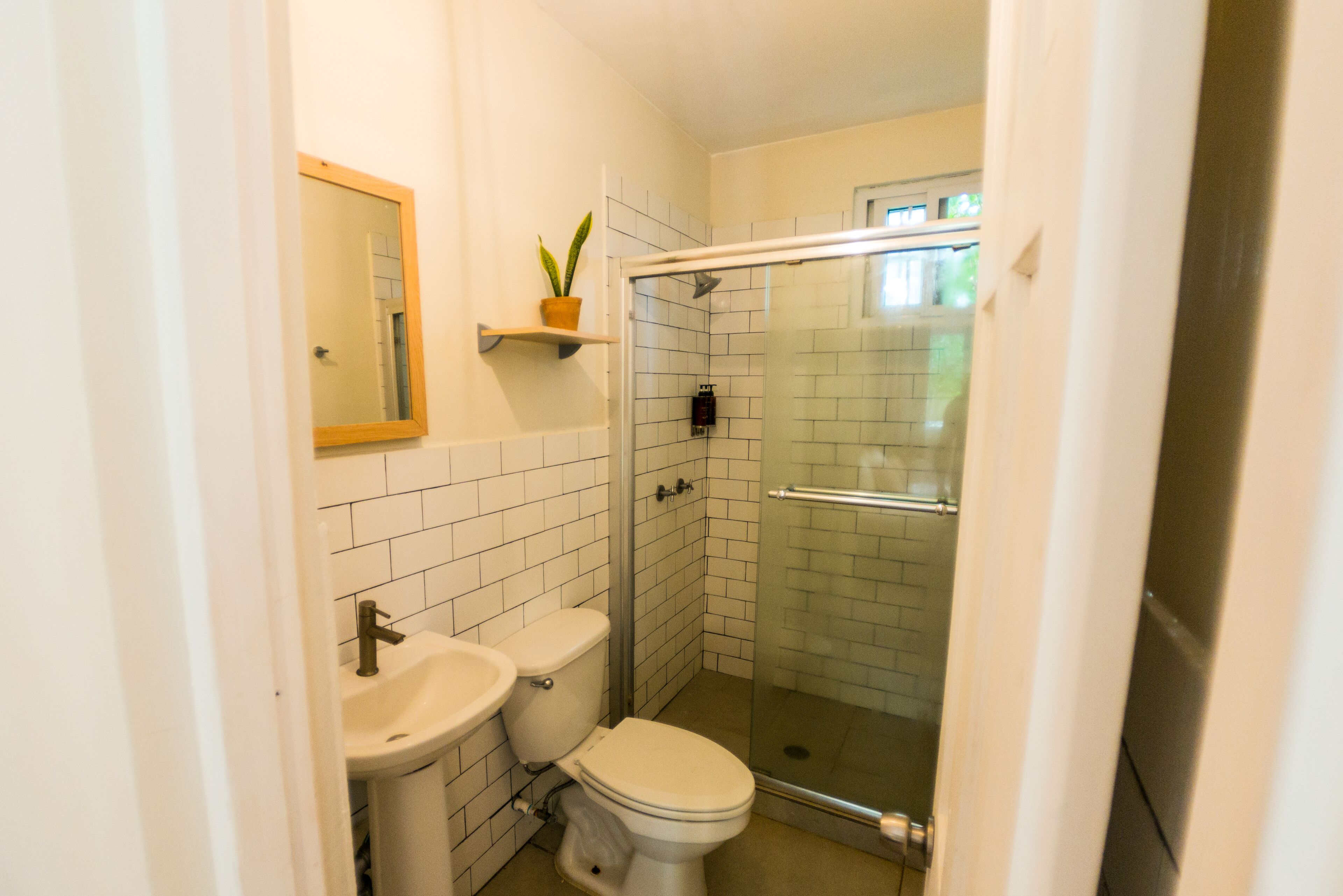 Un baño pequeño con paredes blancas, inodoro, lavamanos y ducha con mampara de vidrio.