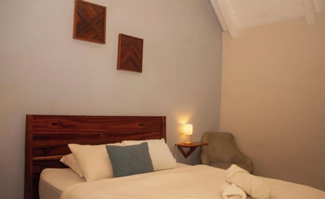 A neatly made bed with a wooden headboard, a bedside lamp, and a chair.
