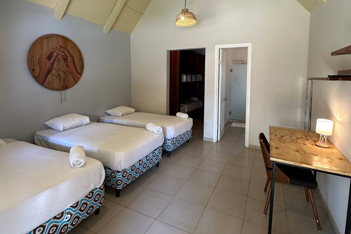 A room with two beds, a wooden table, and a hanging light fixture.