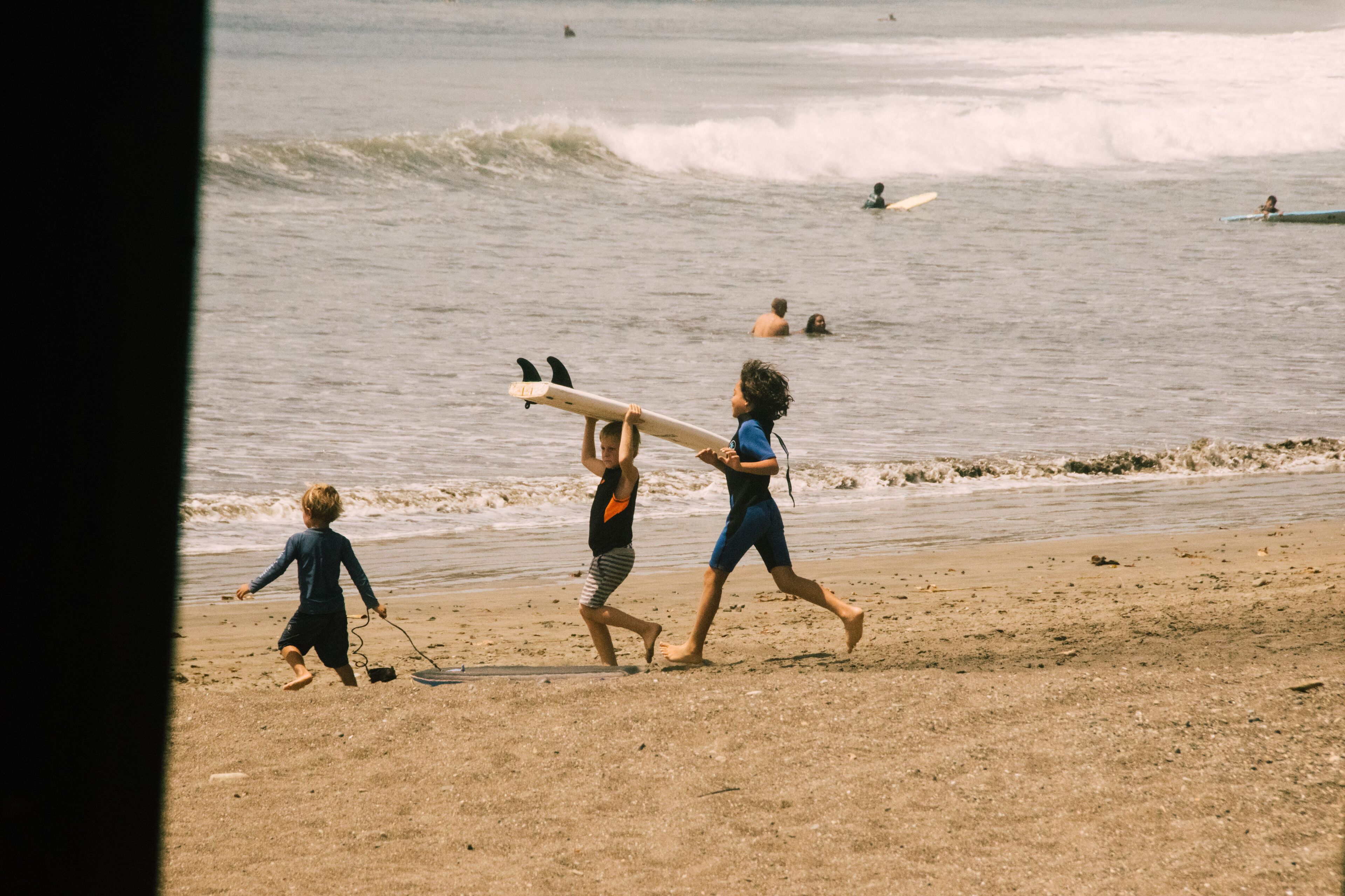 Escena de playa con niños jugando y sosteniendo tablas de surf.