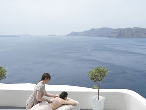 A massage therapy session on a balcony overlooking a scenic view of the sea and cliffs.