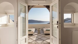 Un umbral abierto que da a un balcón con vista al mar y una isla distante.