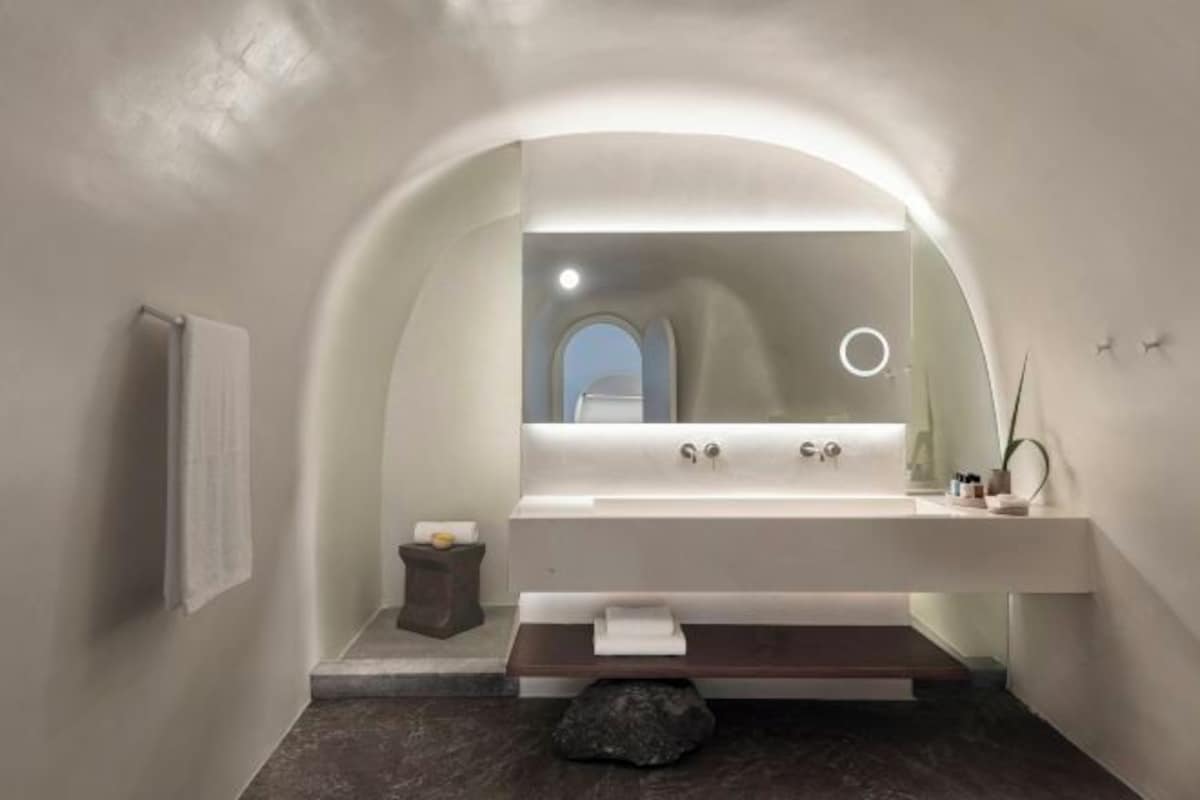 A modern bathroom with a curved mirror, a sink, and a small bench.