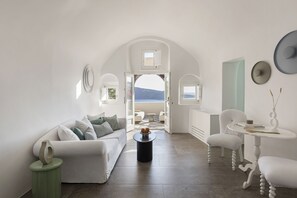 A modern, white-themed living room with a view of the sea, a round coffee table, and a white sofa with cushions.