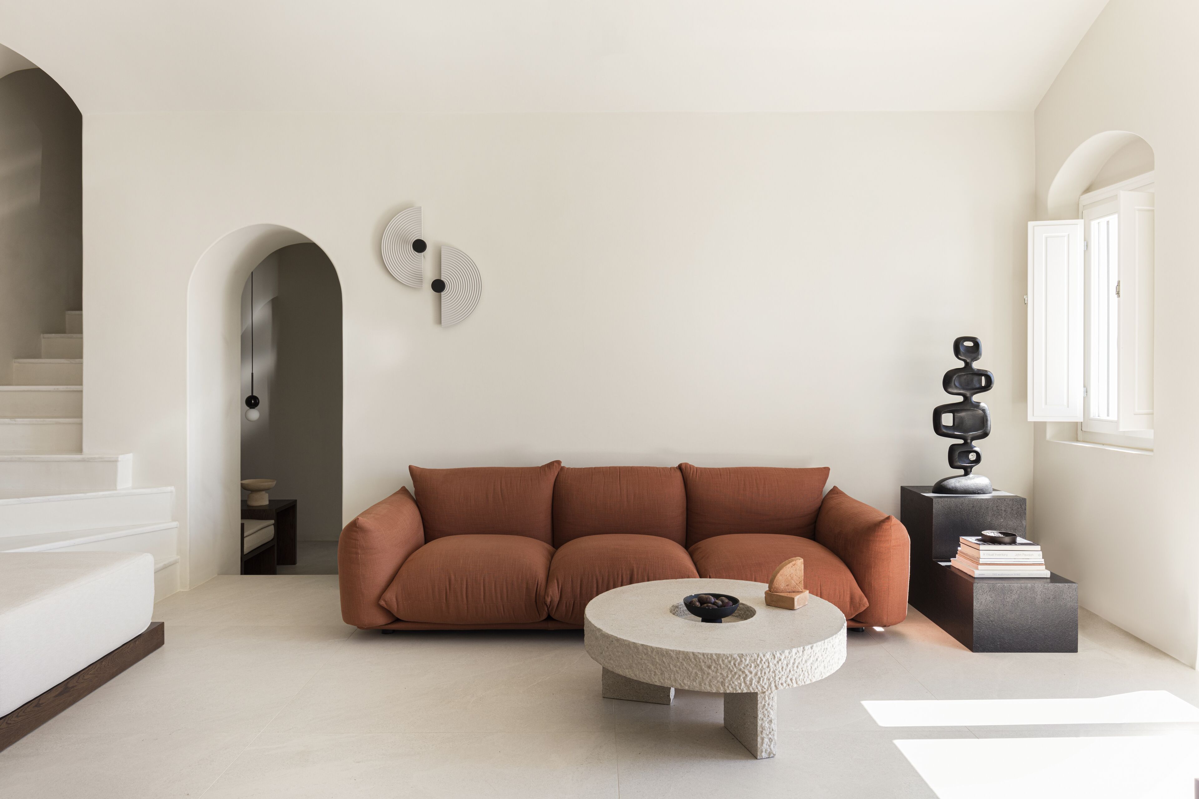 Una sala de estar moderna con un sofá marrón, una mesa de centro redonda y una escalera que lleva a un nivel superior.