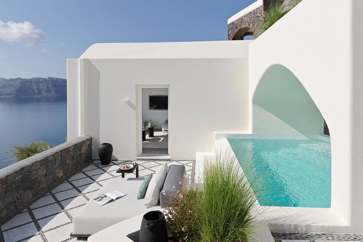A modern outdoor seating area with a pool, overlooking a body of water and a mountainous landscape.