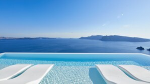 An infinity pool with clear blue water and white lounge chairs, overlooking a calm sea and distant islands. - Canaves Oia Suites - Small Luxury Hotels of the World (Santorini)