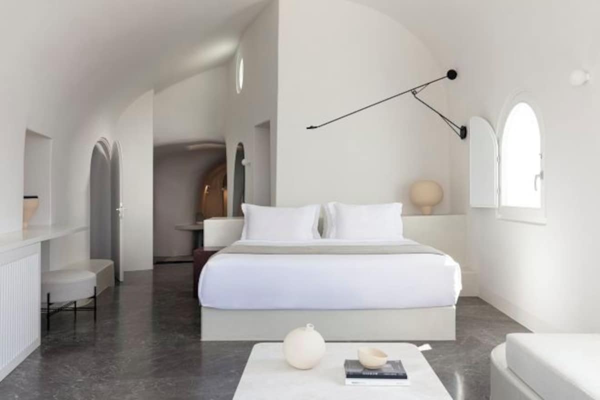A modern bedroom with a large bed, a bedside table, a floor lamp, and a view of a hallway.