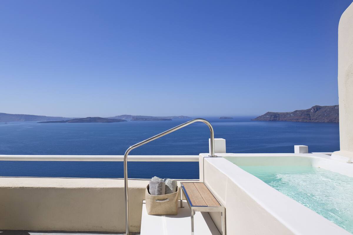 A balcony with a view of the sea, a hot tub, and a towel basket.