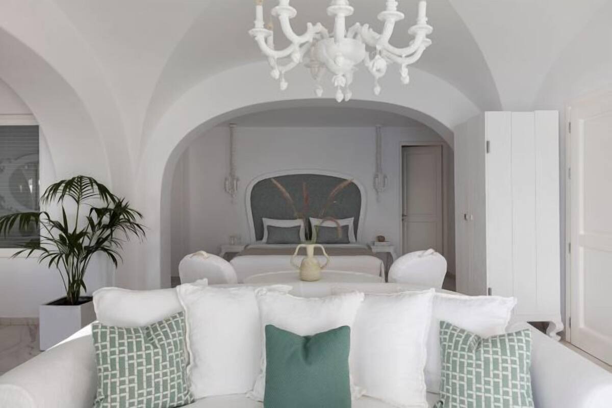 A modern hotel room with a white sofa, a chandelier, and a large mirror.