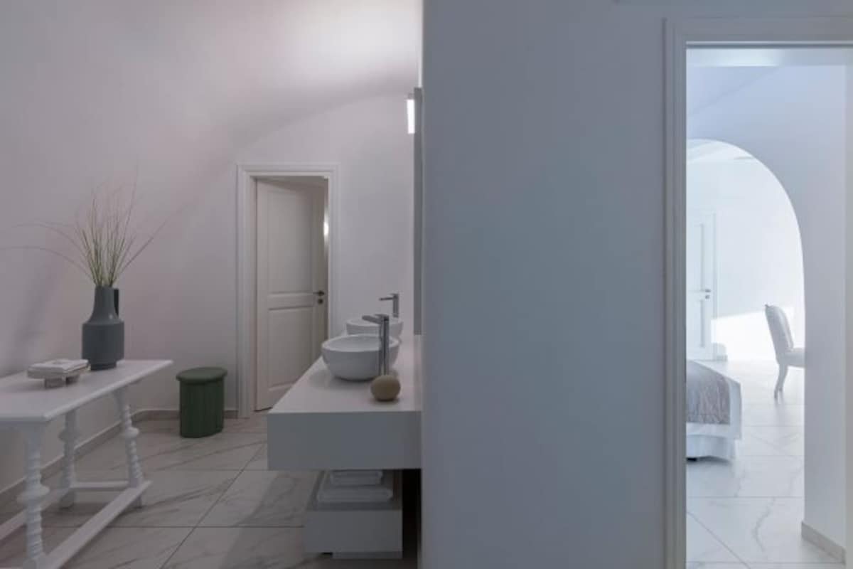 A modern bathroom with a white vanity, a large sink, and a door leading to a bedroom.