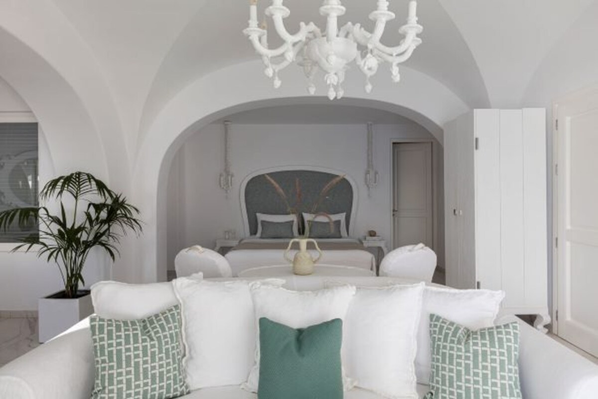 A modern hotel room with a white sofa, a chandelier, and a large mirror.